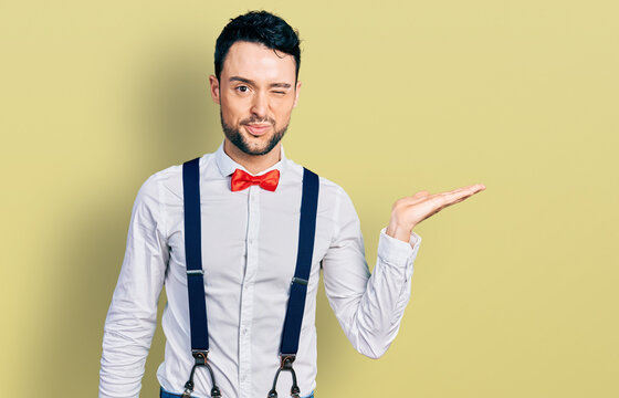 Hispanic man with beard presenting with open palm winking looking at the camera with sexy expression, cheerful and happy face.