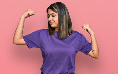 Young hispanic girl wearing casual purple t shirt showing arms muscles smiling proud. fitness concept.