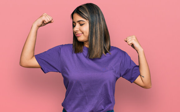 Young Hispanic Girl Wearing Casual Purple T Shirt Showing Arms Muscles Smiling Proud. Fitness Concept.