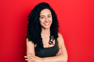 Young hispanic woman with curly hair wearing casual style with sleeveless shirt happy face smiling with crossed arms looking at the camera. positive person.