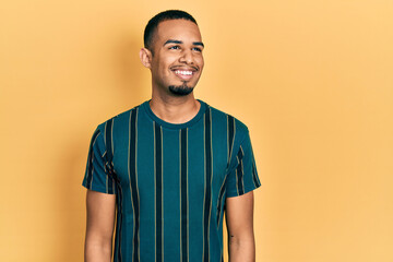 Young african american man wearing casual clothes looking away to side with smile on face, natural...