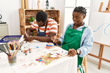 African american painter couple smiling happy painting pottery sitting on the table at art studio.