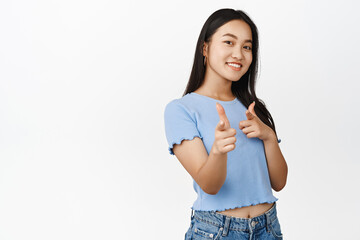 Bang. Smiling asian girl pointing finger pistols at camera, choosing you, recruiting people,...