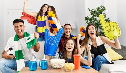 Group of young friends watching and supporting soccer match at home.