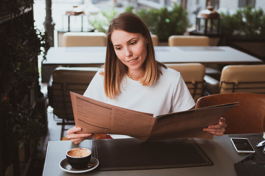 Stylish young woman in street cafe reading menu