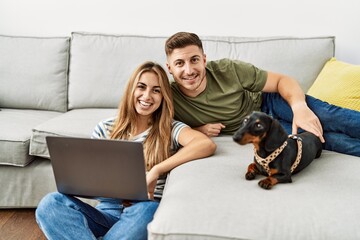 Young hispanic couple smiling happy using laptop sitting on the sofa  with dog at home.