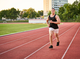 Obraz premium Young muscular fit male sprinter running on a red running track - Fitness and wellness concept with a millennial runner - Copyspace on the photo's left side