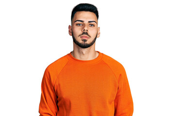 Obraz premium Young hispanic man with beard wearing casual orange sweater relaxed with serious expression on face. simple and natural looking at the camera.