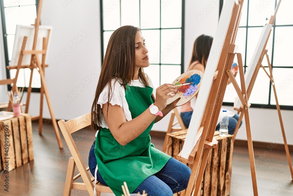 Sticker young hispanic artist women painting on canvas at art studio relaxed with serious expression on face