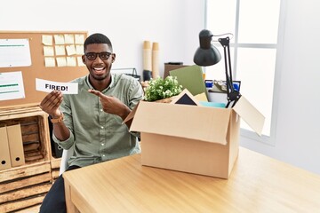 Young african american businessman holding fired banner at the office smiling happy pointing with hand and finger