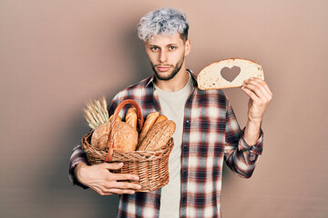 Young hispanic man with modern dyed hair holding wicker basket with bread and loaf with heart...