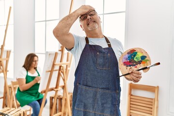 Middle age hispanic man at art studio stressed and frustrated with hand on head, surprised and...