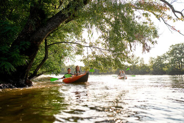 Joyful young adventurous people having fun together while kayaking on the river surrounded by trees