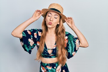 Young caucasian woman wearing summer hat looking at the camera blowing a kiss being lovely and sexy. love expression.