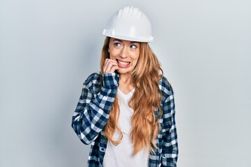 Young caucasian woman wearing architect hardhat looking stressed and nervous with hands on mouth biting nails. anxiety problem.