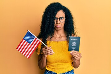 Middle age african american woman holding united states flag and passport depressed and worry for...