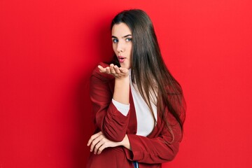 Young brunette teenager wearing business jacket looking at the camera blowing a kiss with hand on air being lovely and sexy. love expression.