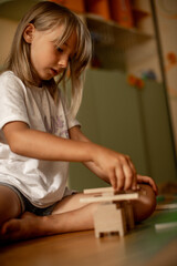 girl 7 years old plays at home with toys. Girl builds a tower from wooden sticks