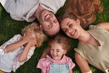 Top view of happy parents with playful little kids lying on green grass in summer park