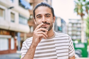 Young hispanic man smiling confident smoking cigarette at street