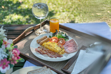 Fresh and delicious breakfast outdoor in the morning with eggs, bacon, hams, sausages and juice at the resort in Chiangmai, Thailand. Green grasses visible in the background