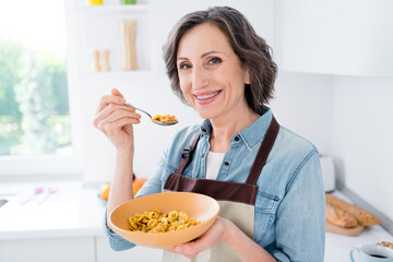 Photo of cheerful positive joyful old woman hold hand plate spoon cereal indoors inside house home...