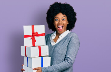 Young african american woman holding gifts celebrating crazy and amazed for success with open eyes screaming excited.