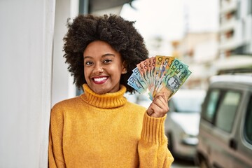 Young african american girl smiling happy holding australian dollars at the city.