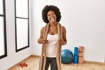 Young african american woman with afro hair at the gym training with battle ropes sticking tongue out happy with funny expression. emotion concept. © Krakenimages.com