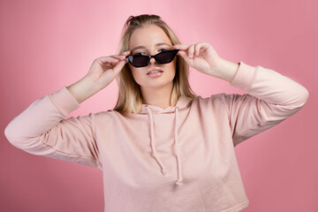 Stylish young and trendy blonde in a pink oversized hoodie and black sunglasses,