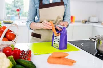 Cropped photo of mature lady cut carrot wear apron jeans shirt at kitchen alone