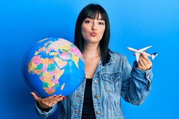 Young hispanic woman holding paper toy and world ball looking at the camera blowing a kiss being lovely and sexy. love expression.