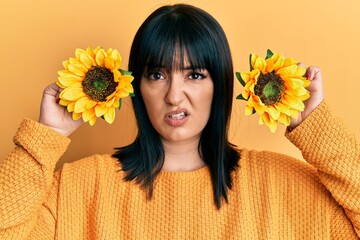 Young hispanic woman holding sunflowers over eyes clueless and confused expression. doubt concept.