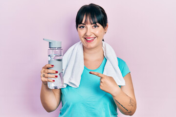 Young hispanic woman wearing sportswear holding water bottle smiling happy pointing with hand and finger