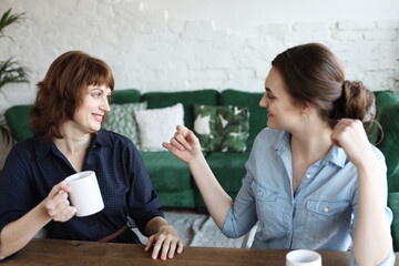 Beautiful mature mother and her adult daughter are drinking coffee