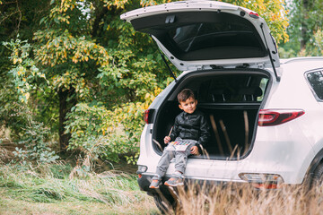 A child is sitting in the trunk of a car SUV or crossover with gouache paints, a car in the autumn...