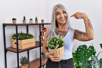 Middle age grey-haired woman holding green plant pot at home smiling cheerful showing and pointing with fingers teeth and mouth. dental health concept.