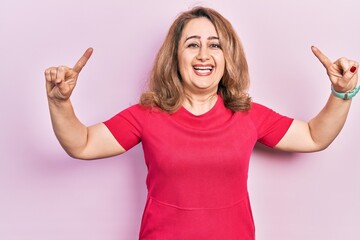 Middle age caucasian woman wearing casual clothes smiling amazed and surprised and pointing up with fingers and raised arms.