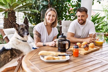 Young couple with dog smiling happy having breakfast at terrace.