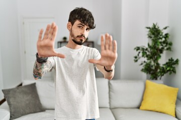 Hispanic man with beard at the living room at home doing frame using hands palms and fingers, camera perspective