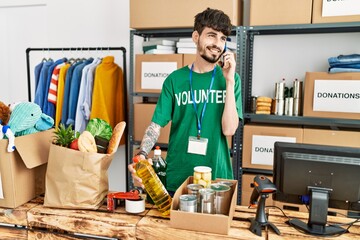 Young hispanic man wearing volunteer uniform talking on the smartphone at charity center.