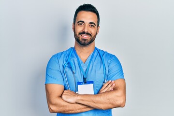 Handsome hispanic man with beard wearing doctor uniform happy face smiling with crossed arms looking at the camera. positive person.