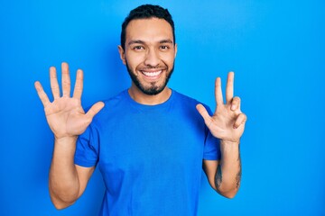Naklejka premium Hispanic man with beard wearing casual blue t shirt showing and pointing up with fingers number eight while smiling confident and happy.