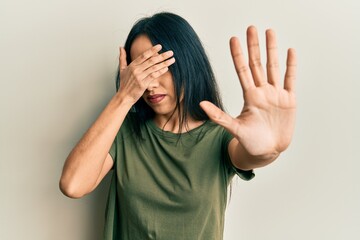 Young hispanic girl wearing casual t shirt covering eyes with hands and doing stop gesture with sad and fear expression. embarrassed and negative concept.