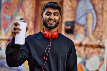Young arab man smiling confident holding graffiti spray at street