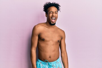 Young african american man with beard wearing swimsuit winking looking at the camera with sexy expression, cheerful and happy face.