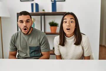 Young latin couple wearing casual clothes sitting on the table scared and amazed with open mouth...