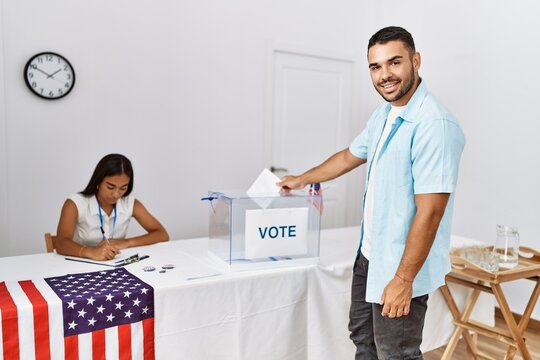 Young american voter man smiling happy putting vote in ballot box at electoral college.