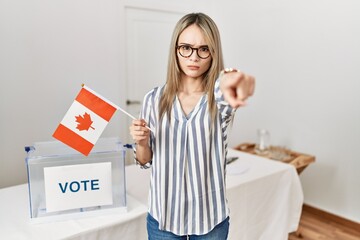 Asian young woman at political campaign election holding canada flag pointing with finger to the camera and to you, confident gesture looking serious