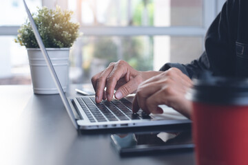 Business man hands typing, working on laptop computer on table at home office, close up